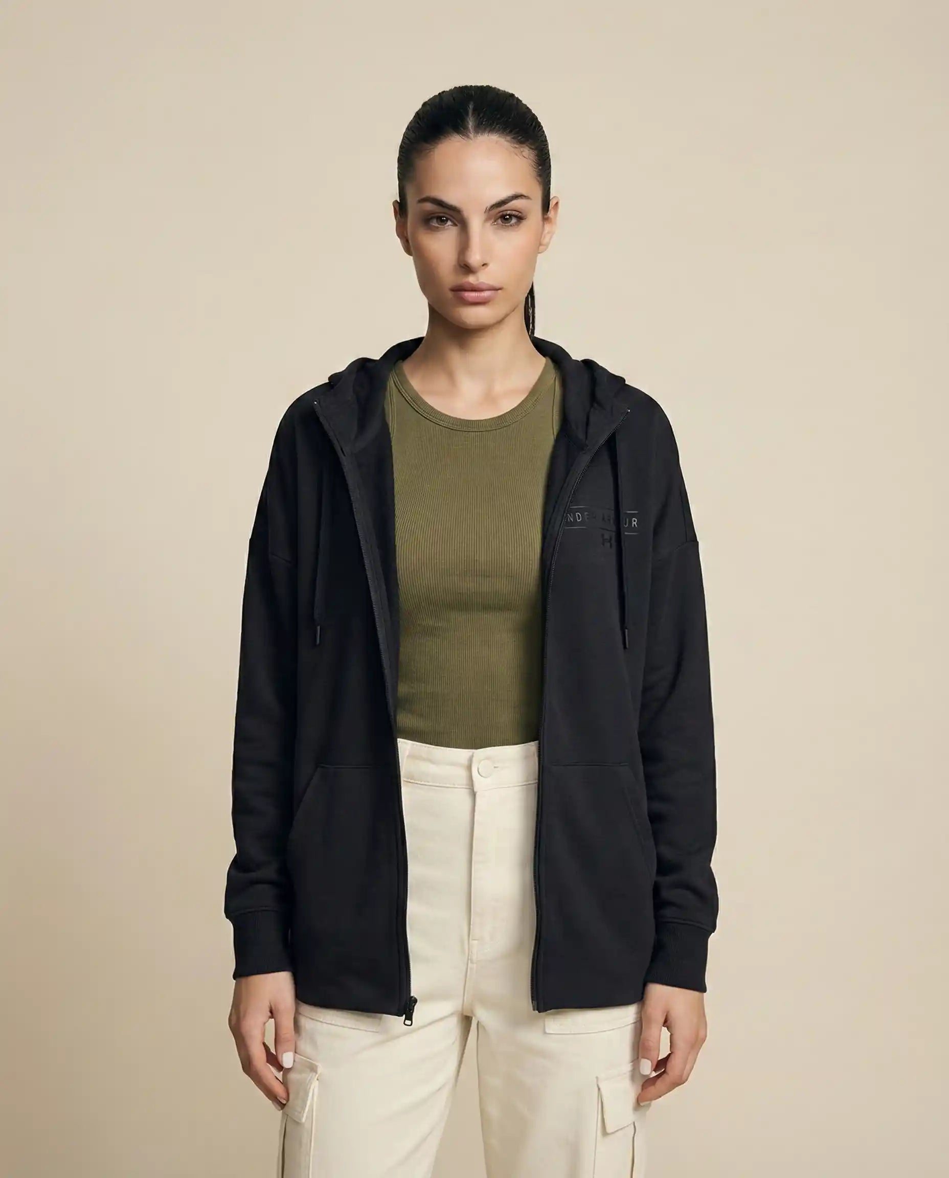 Woman wearing black zip-up hoodie, olive green shirt, beige cargo pants, neutral background