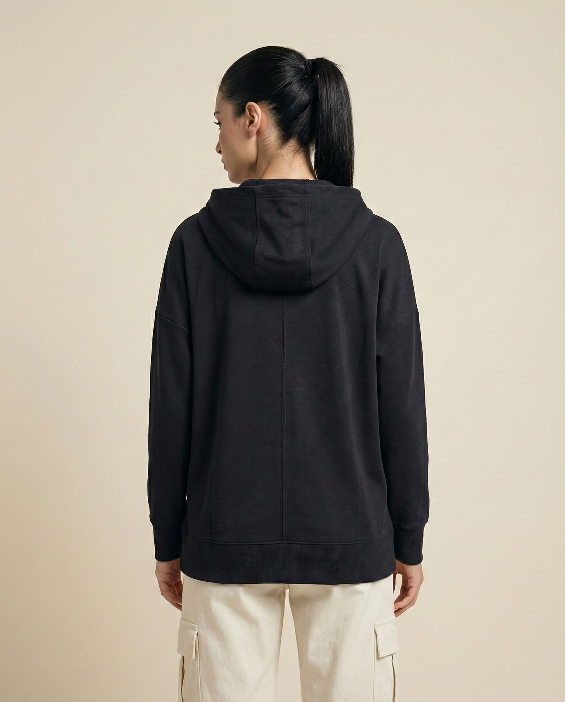 Woman in black hoodie and beige cargo pants, back view, neutral background
