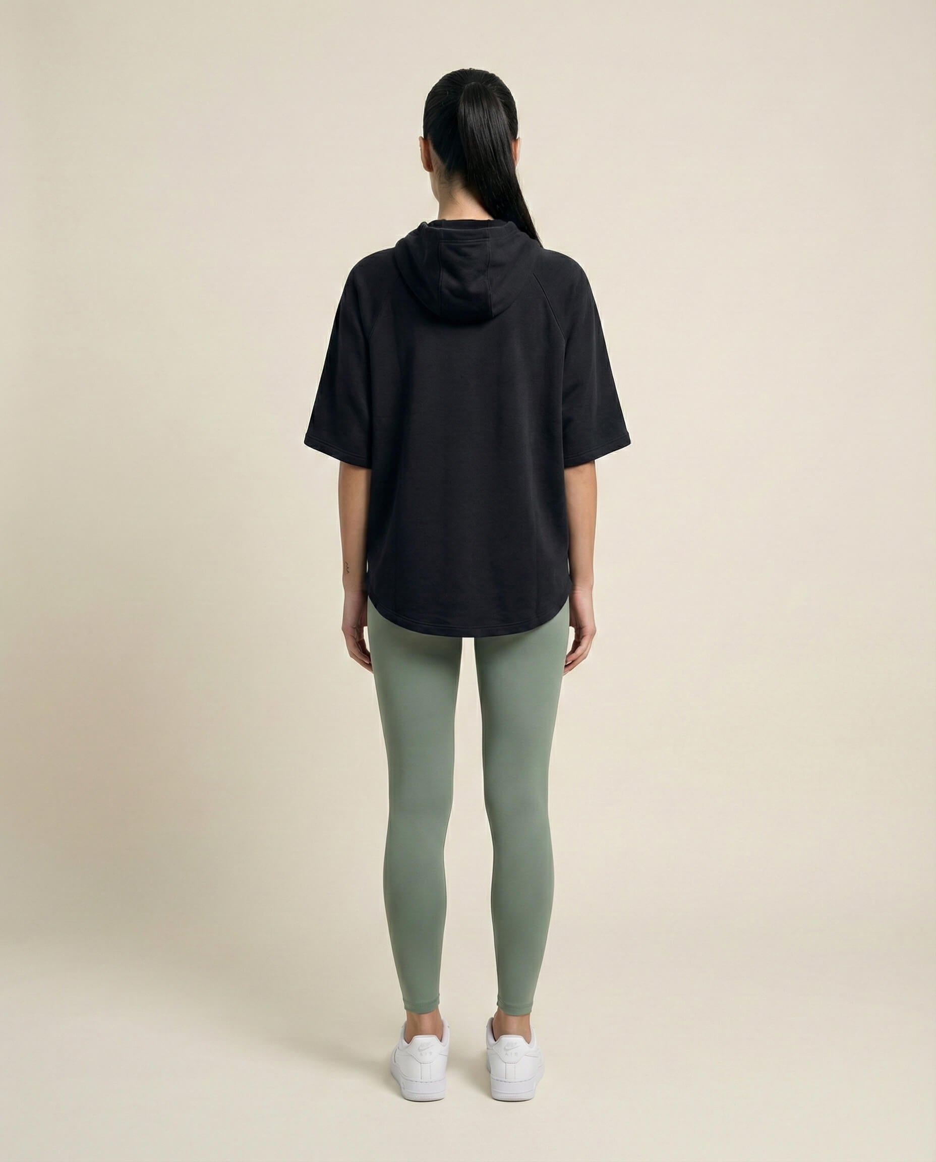 Woman in a black short-sleeve hoodie, sage green leggings, and white sneakers, back view