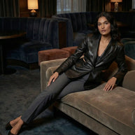 Woman in black leather blazer and gray pants lounging on a velvet sofa in a stylish lounge