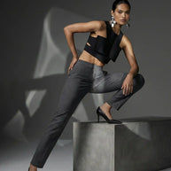 Woman in a black crop top, gray dress pants, and heels posing in a modern studio.