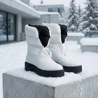 Pair of white winter boots with black soles displayed outdoors on snowy concrete