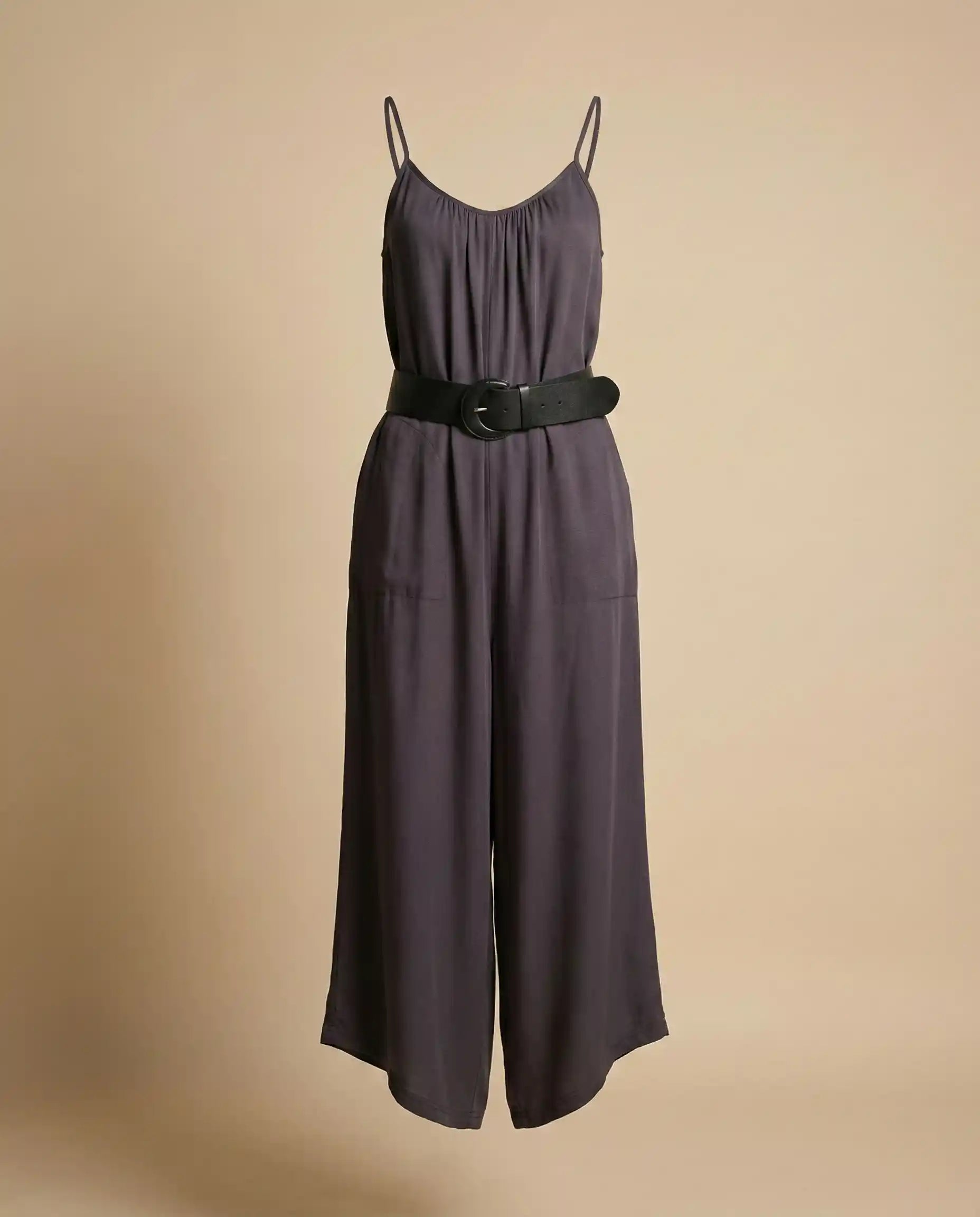 Sleeveless dark gray jumpsuit with thin straps and wide black belt on beige background