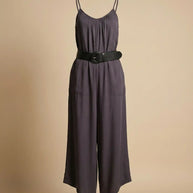Sleeveless dark gray jumpsuit with thin straps and wide black belt on beige background