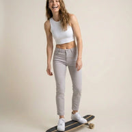 Smiling woman in white crop top and light jeans standing on skateboard indoors