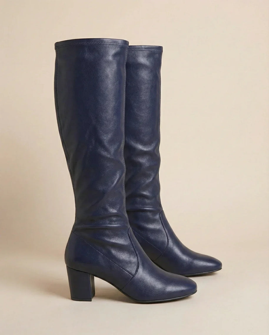 Pair of navy blue knee-high heeled boots with round toes and block heels on neutral background
