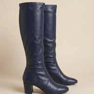 Pair of navy blue knee-high heeled boots with round toes and block heels on neutral background