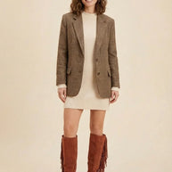 Woman wearing plaid blazer, cream sweater dress, and brown fringe knee-high boots.
