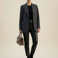 Woman in gray blazer, black top, leather pants, ankle boots, carrying brown handbag
