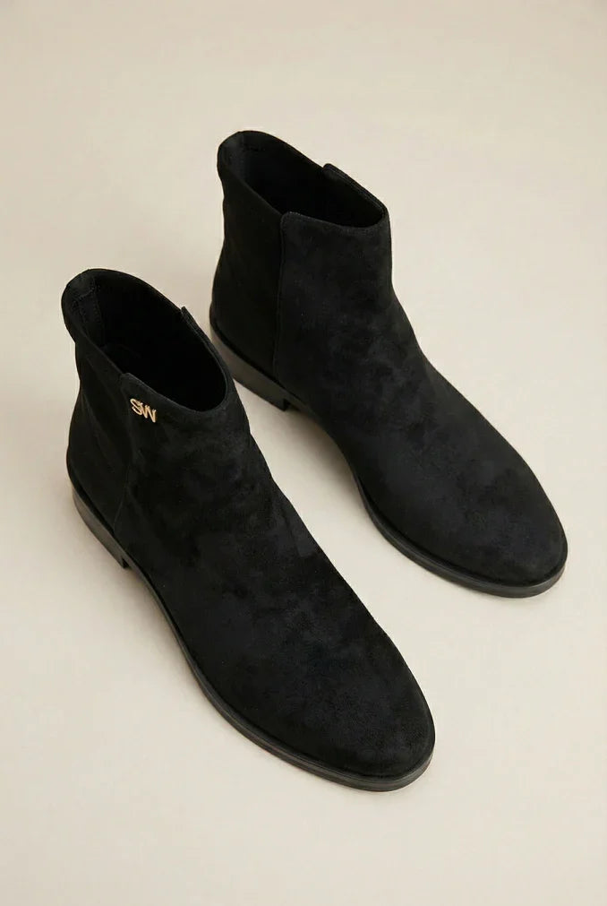 Pair of black suede ankle boots with flat soles on a neutral background