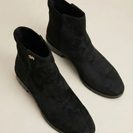 Pair of black suede ankle boots with flat soles on a neutral background