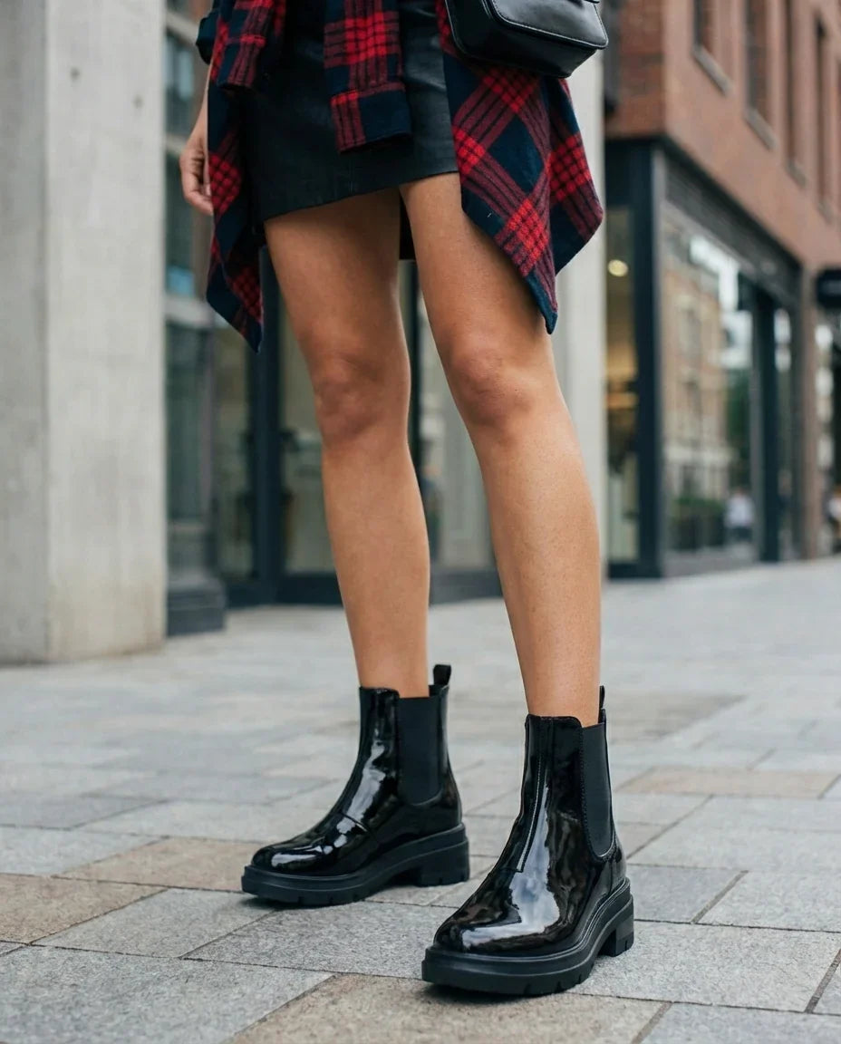 Woman wearing shiny black ankle boots, black skirt, and red plaid shirt on city street