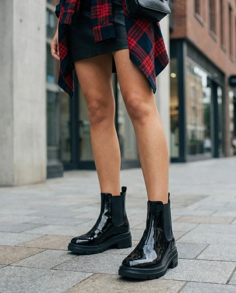 Woman wearing shiny black ankle boots, black skirt, and red plaid shirt on city street