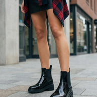 Woman wearing shiny black ankle boots, black skirt, and red plaid shirt on city street