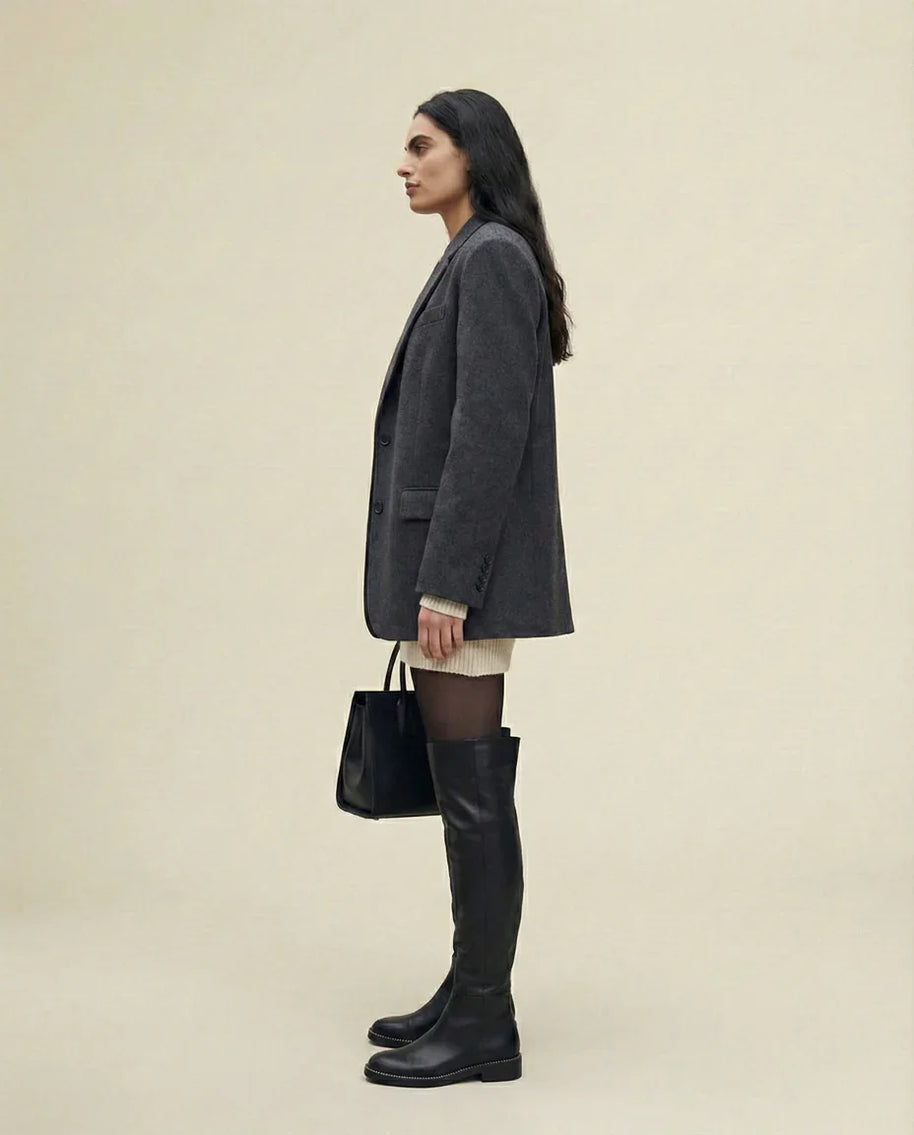 Woman in a gray blazer, sweater dress, black over-the-knee boots, holding a tote bag
