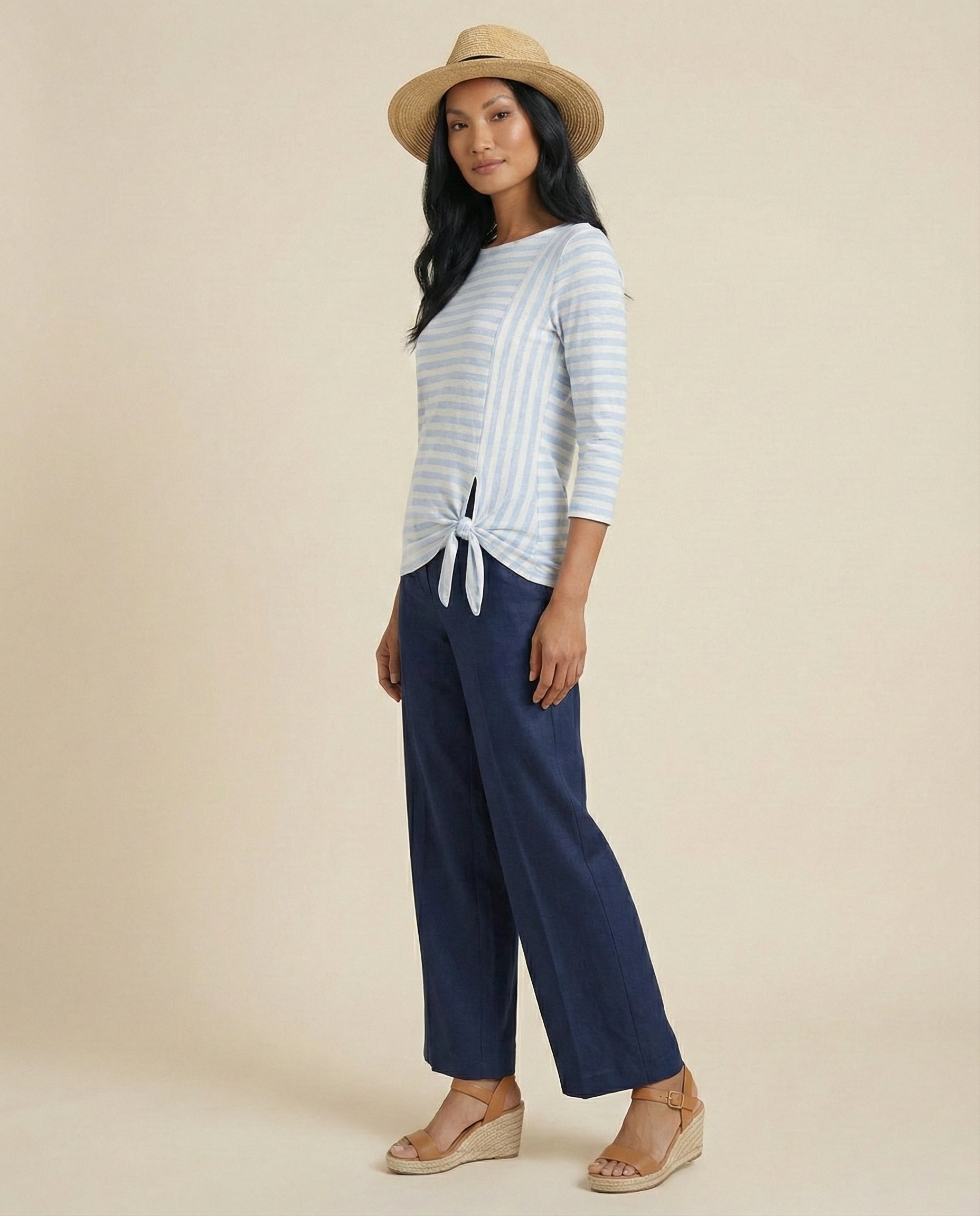 Woman in straw hat, blue striped tie-front top, wide-leg navy pants, wedge sandals