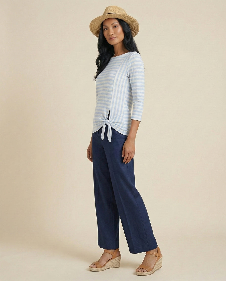 Woman in straw hat, blue striped tie-front top, wide-leg navy pants, wedge sandals