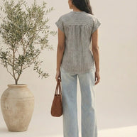 Woman in striped short-sleeve blouse and light blue jeans holding woven bag, standing by potted plant