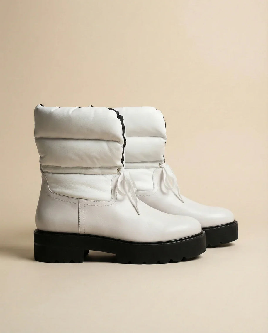 White winter boots with padded uppers and black chunky soles on beige background