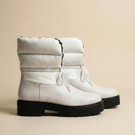 White winter boots with padded uppers and black chunky soles on beige background