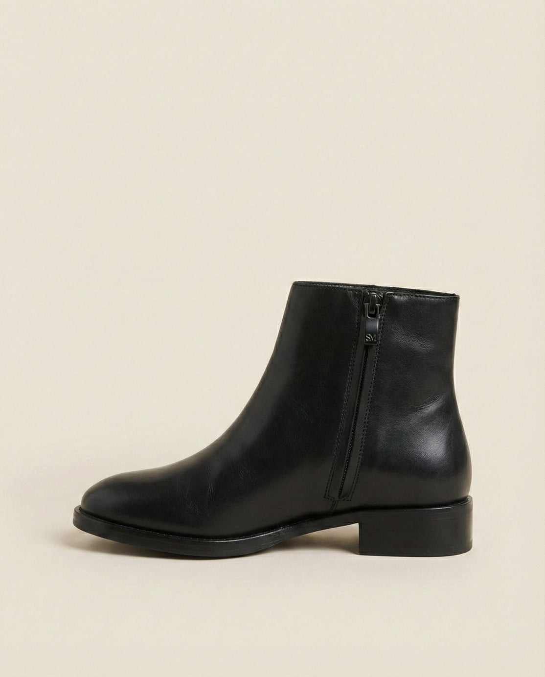 Black leather ankle boot with side zipper on beige background