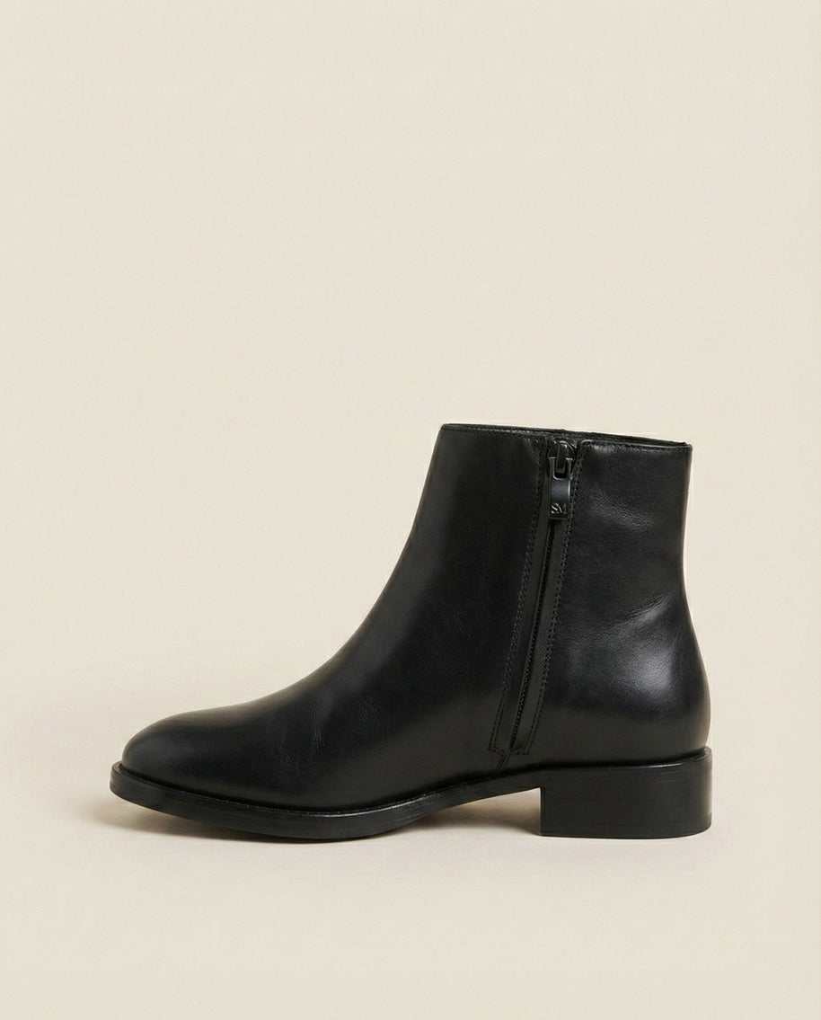 Black leather ankle boot with side zipper on beige background