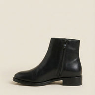 Black leather ankle boot with side zipper on beige background