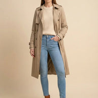 Woman wearing a beige trench coat, knit sweater, blue skinny jeans, and brown ankle boots