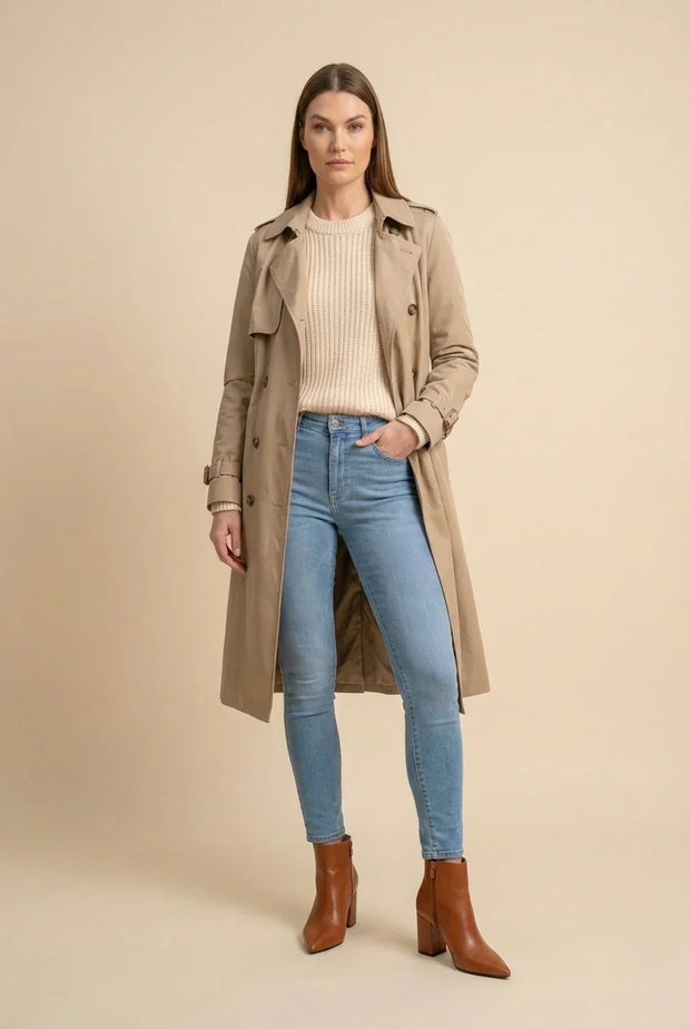 Woman wearing a beige trench coat, knit sweater, blue skinny jeans, and brown ankle boots