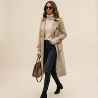 Woman in beige trench coat, turtleneck sweater, skinny jeans, and ankle boots holding handbag