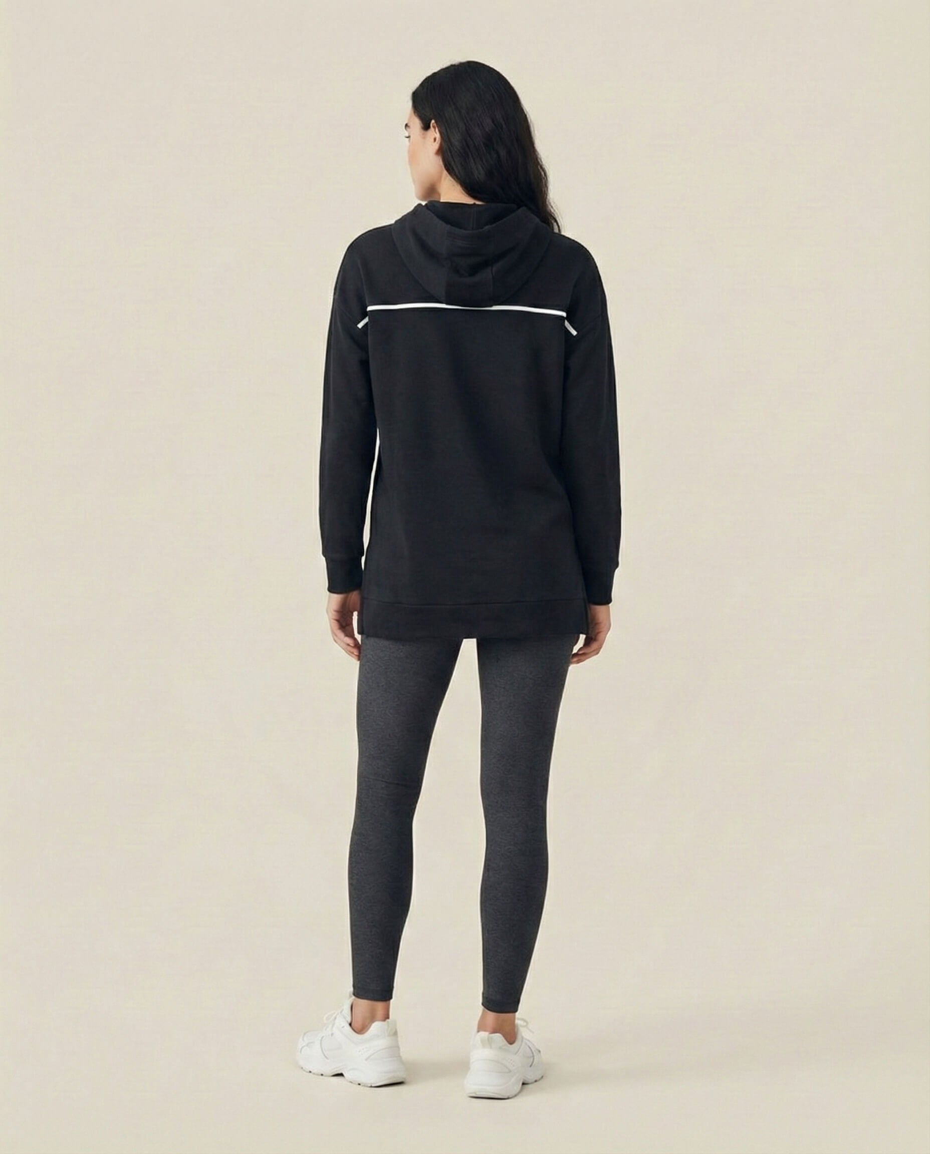 Woman in black hoodie and gray leggings, white sneakers, neutral background