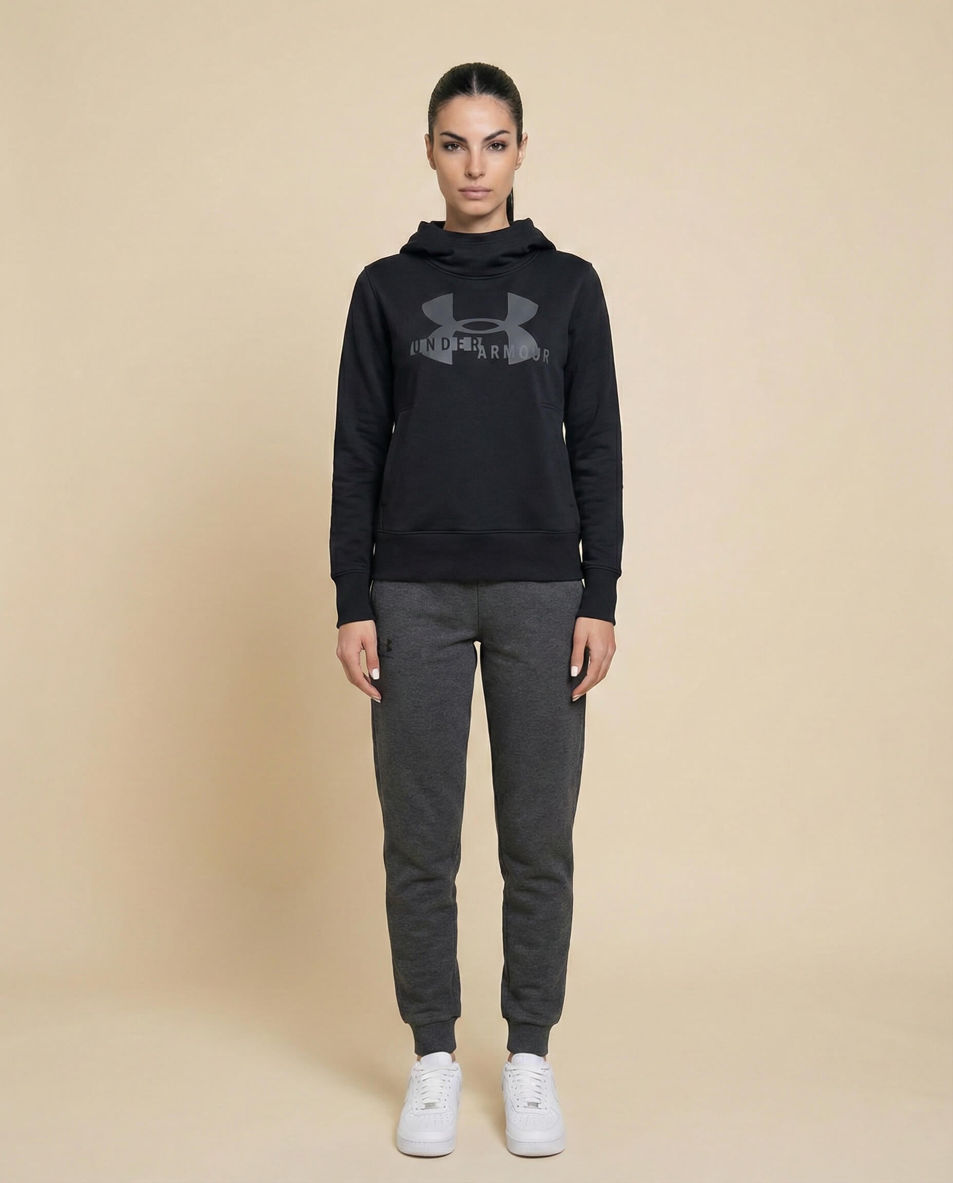 Woman wearing black hoodie and dark gray joggers with white sneakers on beige background