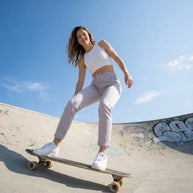 Woman skateboarding in a skatepark on a sunny day, wearing white tank top and light pants