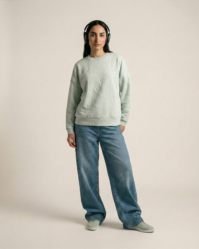 Woman wearing headphones, light green sweatshirt, wide-leg jeans, and sneakers