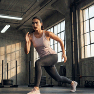 Woman in light pink athletic tank top and gray leggings in gym, running stance