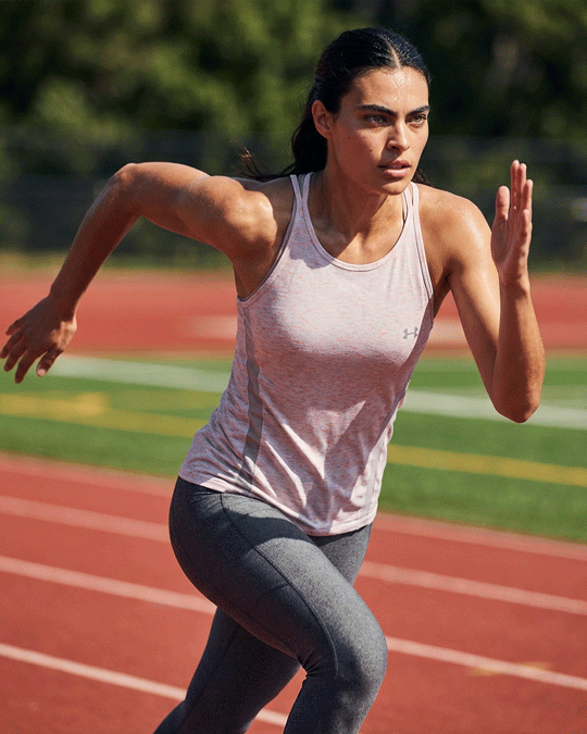 Woman running on outdoor track wearing light pink athletic tank top and gray leggings