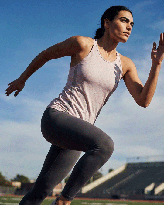 Woman running outdoors in a light pink athletic tank top and gray leggings on a track field