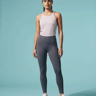 Woman in light pink athletic tank top and gray leggings posing on a light blue background