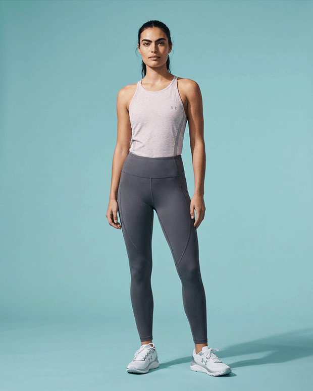 Woman in light pink athletic tank top and gray leggings posing on a light blue background