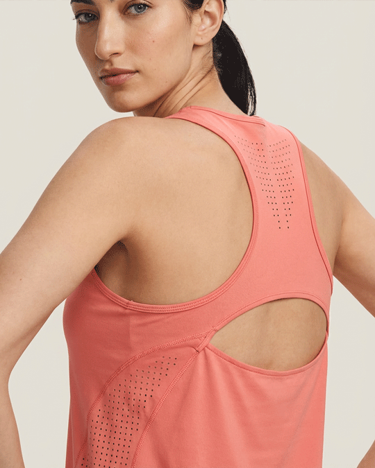 Woman wearing salmon pink athletic tank top with laser-cut ventilation on back