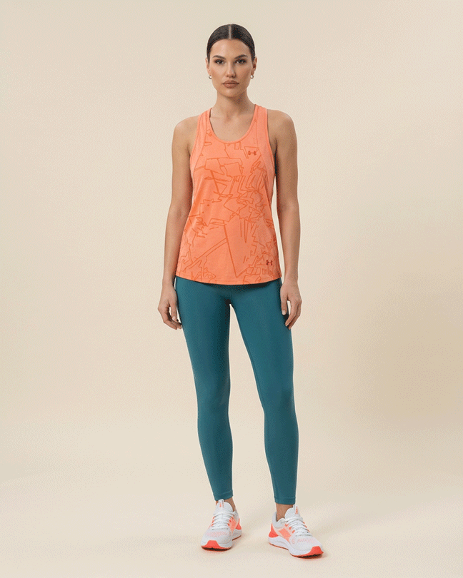 Woman wearing an orange patterned athletic tank top, teal leggings, and white sneakers