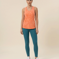 Woman wearing an orange patterned athletic tank top, teal leggings, and white sneakers