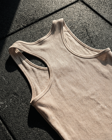 Beige athletic tank top on textured dark floor in sunlight, racerback design, ribbed fabric