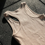 Beige athletic tank top on textured dark floor in sunlight, racerback design, ribbed fabric