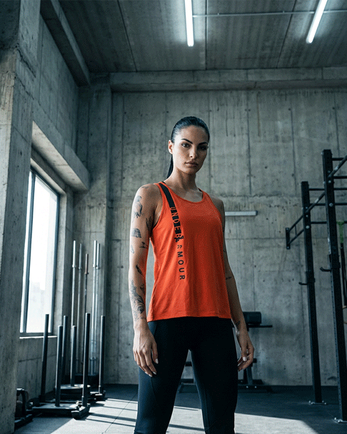 Woman in a red Under Armour tank top and black leggings standing in a modern gym