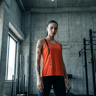 Woman in a red Under Armour tank top and black leggings standing in a modern gym