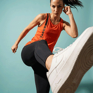 Woman in red Under Armour tank top and black leggings kicking, athletic wear, blue background