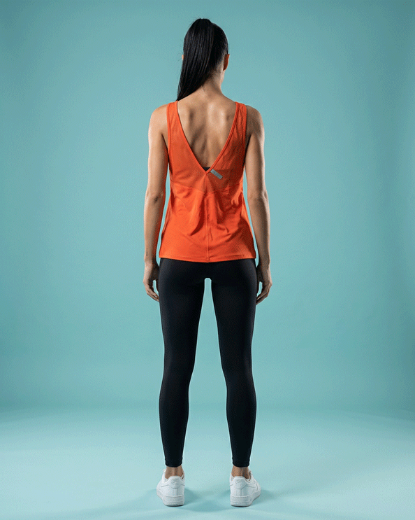 Woman in red Under Armour tank top and black leggings, back view, on blue background