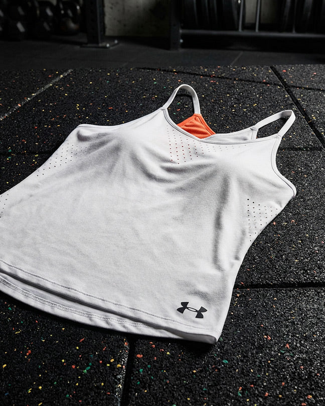 White athletic tank top with orange asymmetric accent and perforated sides on gym floor