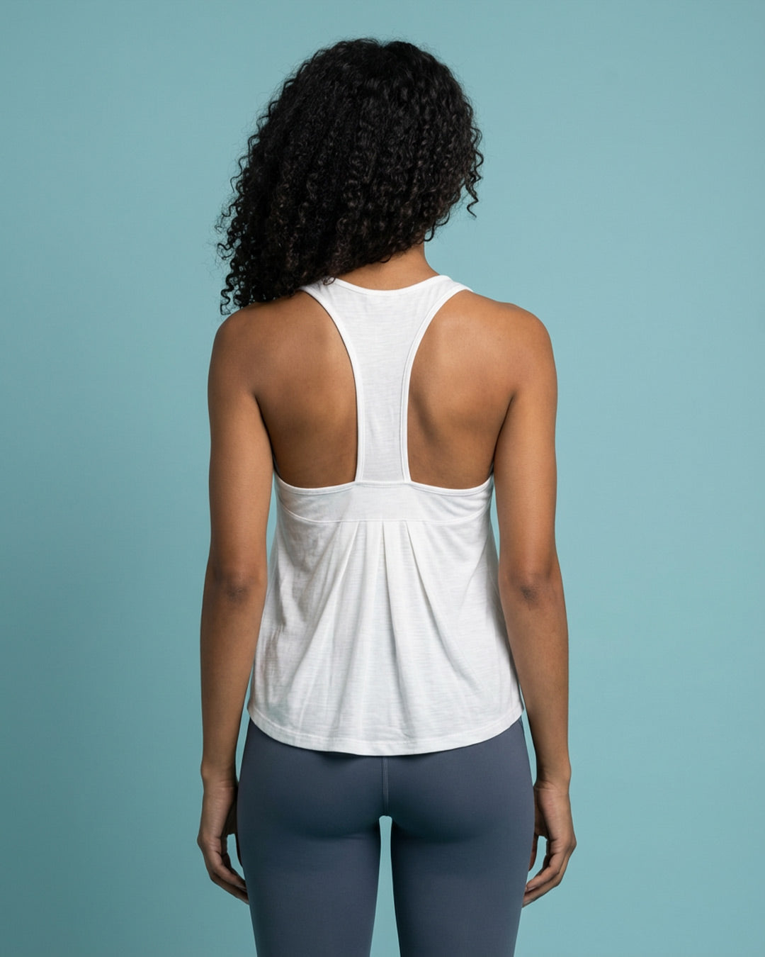Woman wearing white racerback tank top and gray leggings, viewed from the back